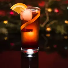 Elegancki drink z cydrem, ozdobiony plasterkiem pomarańczy i skórką, na tle świątecznych światełek.
