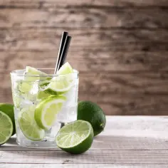 Orzeźwiający drink z limonką i lodem, otoczony świeżymi owocami. Idealny na upalne dni.