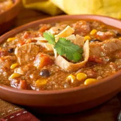 Gęsta zupa z grilla z kurczakiem, kukurydzą i fasolą, ozdobiona chrupiącymi nachos i kolendrą.