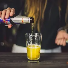 Osoba nalewa do szklanki drink z red bullem.