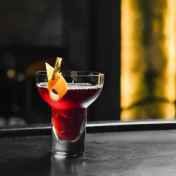 Elegancki drink czarny rusek, ozdobiony skórką pomarańczy, kusi głębokim kolorem na barze.