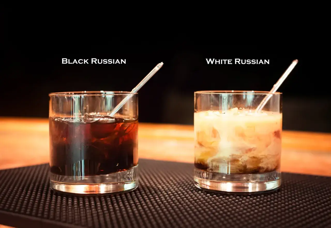 Dwa drinki na blacie: ciemny Black Russian z lodem i jasny White Russian z mlekiem.