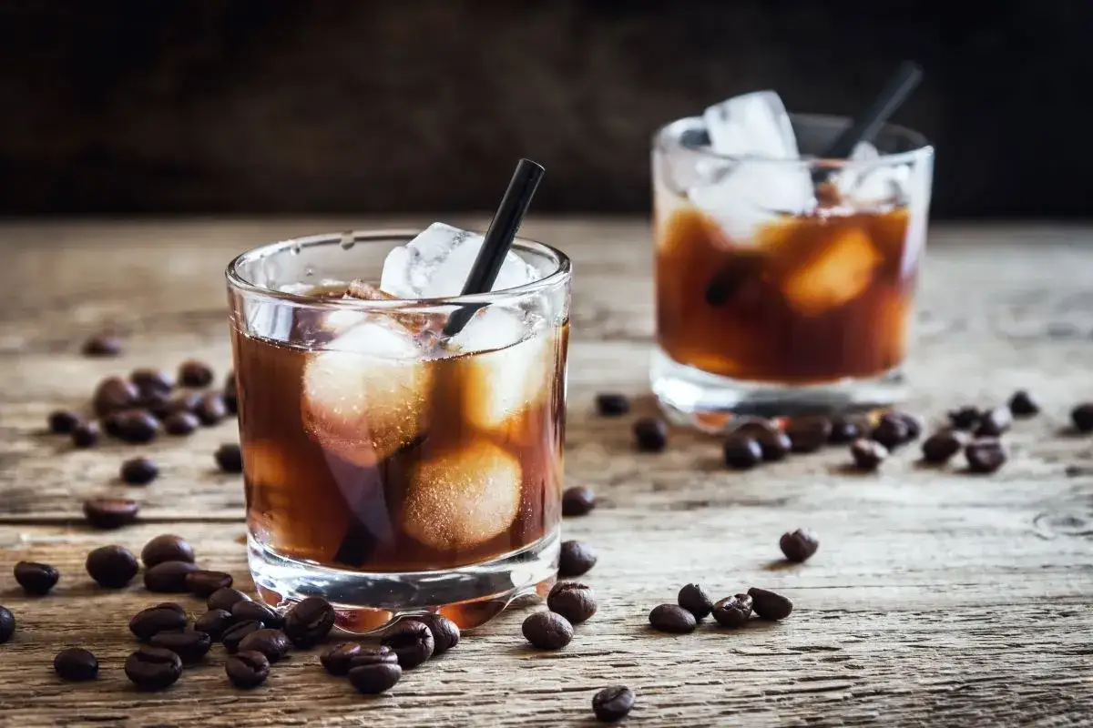 Dwa szklanki z lodem i ciemnym napojem, otoczone ziarnami kawy. Idealny black russian drink na drewnianym blacie.
